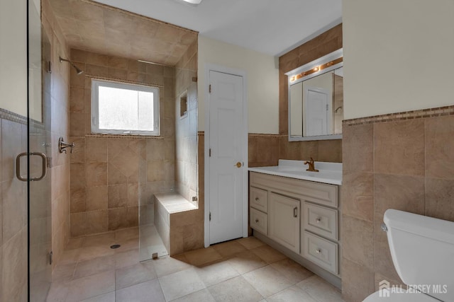 bathroom with toilet, tile walls, a stall shower, and vanity