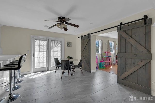 dining space featuring a barn door, baseboards, visible vents, and ceiling fan