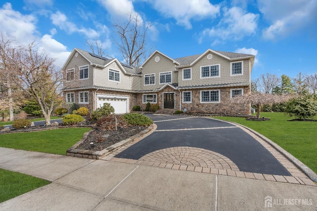 shingle-style home featuring aphalt driveway, an attached garage, stone siding, and a front lawn