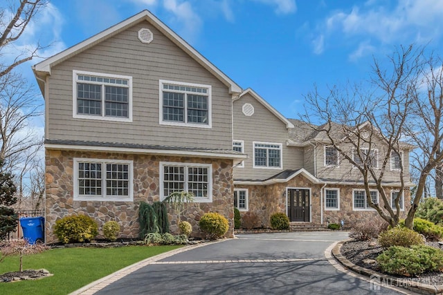 view of front of property with aphalt driveway, stone siding, a front yard, and fence