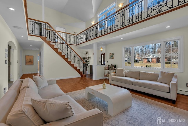 living room featuring baseboards, stairway, a high ceiling, wood finished floors, and ornate columns