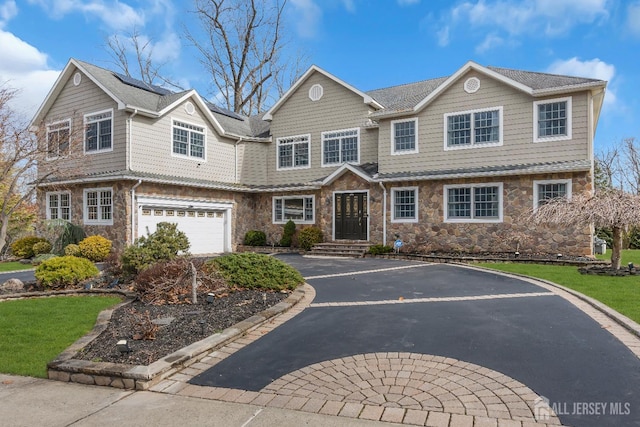 view of front of home with stone siding, solar panels, driveway, and a garage