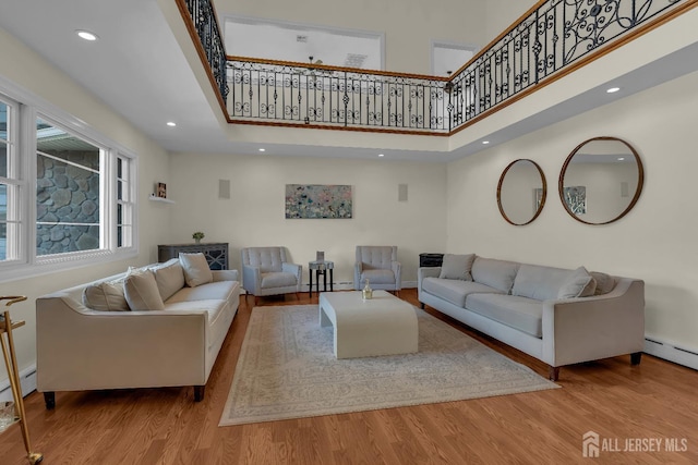 living area featuring baseboard heating, recessed lighting, a high ceiling, and wood finished floors