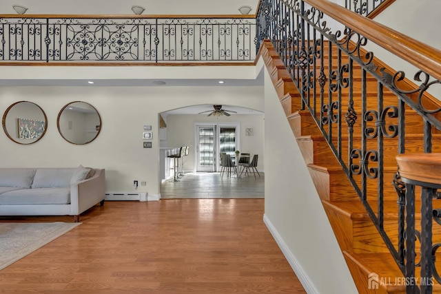 stairway with wood finished floors, baseboards, arched walkways, a towering ceiling, and a baseboard heating unit