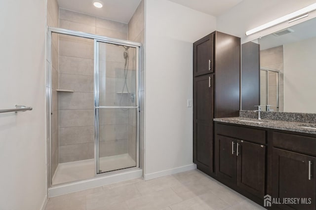 bathroom featuring double vanity, a stall shower, a sink, and baseboards