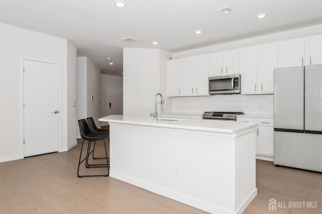 kitchen featuring white cabinets, an island with sink, appliances with stainless steel finishes, light countertops, and a sink