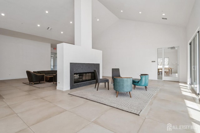 living area with visible vents, a glass covered fireplace, a towering ceiling, and recessed lighting