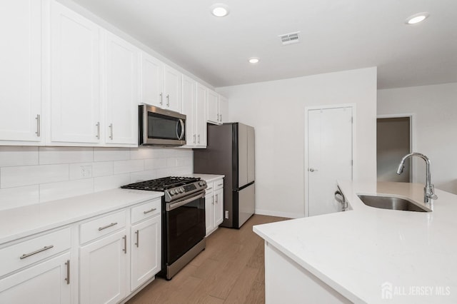 kitchen featuring visible vents, backsplash, appliances with stainless steel finishes, white cabinets, and a sink