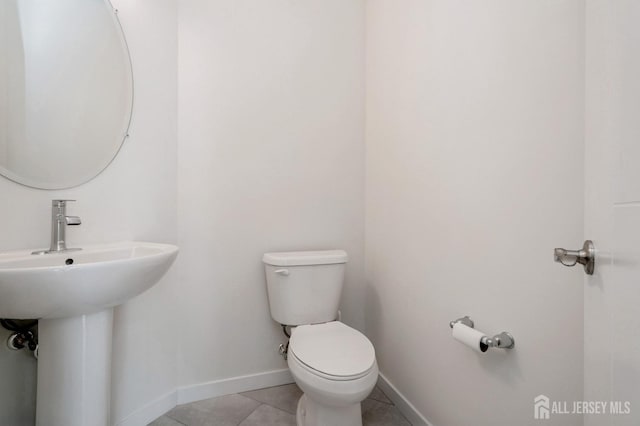 half bath featuring baseboards, a sink, toilet, and tile patterned floors