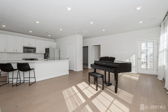 kitchen with white cabinets, light countertops, appliances with stainless steel finishes, light wood-type flooring, and backsplash