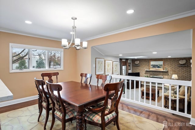 dining area with hardwood / wood-style flooring, ornamental molding, a brick fireplace, and a notable chandelier