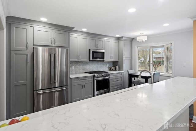 kitchen with gray cabinets, light stone countertops, stainless steel appliances, and decorative backsplash