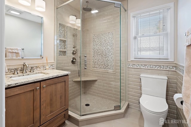 bathroom with tile walls, vanity, walk in shower, tile patterned flooring, and toilet