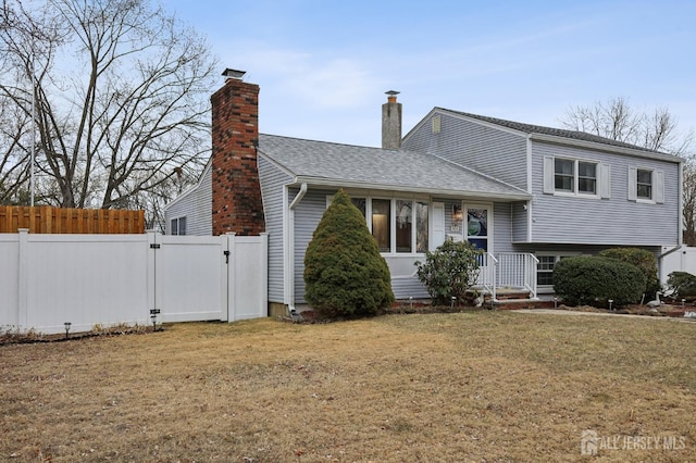 split level home featuring roof with shingles, a chimney, a gate, fence, and a front lawn