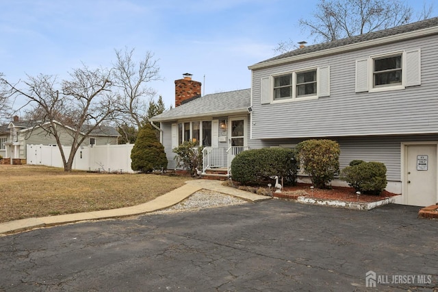 split level home featuring a front yard, fence, and a chimney