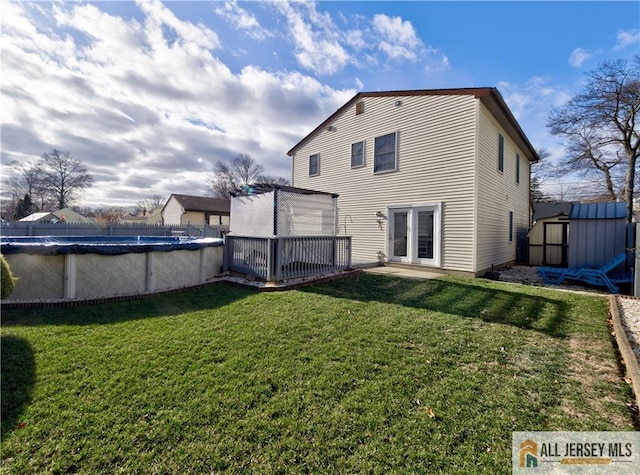 back of house featuring an outbuilding, a yard, a storage shed, a deck, and a covered pool