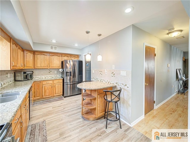 kitchen with a sink, visible vents, hanging light fixtures, open shelves, and stainless steel fridge