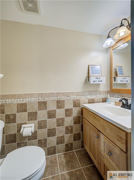 half bathroom with visible vents, toilet, tile patterned floors, vanity, and tile walls