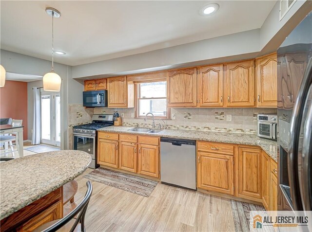 kitchen with sink, light hardwood / wood-style flooring, appliances with stainless steel finishes, pendant lighting, and light stone countertops