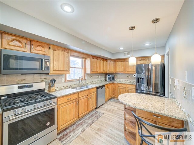 kitchen with sink, decorative light fixtures, light stone countertops, and appliances with stainless steel finishes