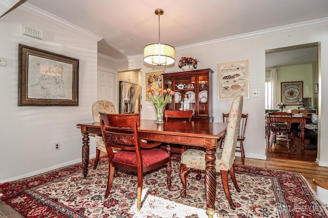 dining area featuring visible vents, crown molding, baseboards, and wood finished floors