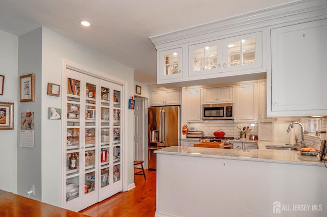 kitchen featuring decorative backsplash, glass insert cabinets, light stone countertops, stainless steel appliances, and a sink