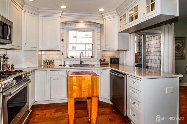 kitchen with dark wood finished floors, appliances with stainless steel finishes, white cabinets, a sink, and a peninsula