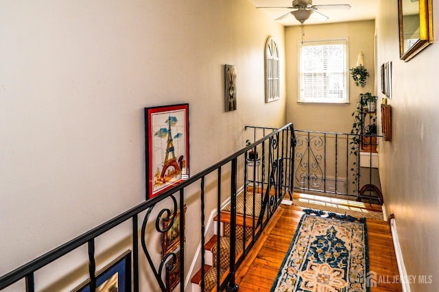 corridor with wood finished floors, an upstairs landing, and baseboards