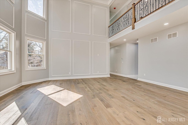 spare room with a decorative wall, a towering ceiling, visible vents, and wood-type flooring