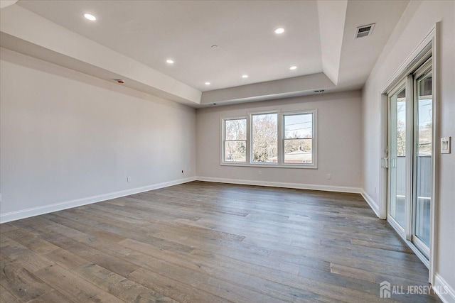 spare room with a wealth of natural light, visible vents, a tray ceiling, and dark wood-style flooring