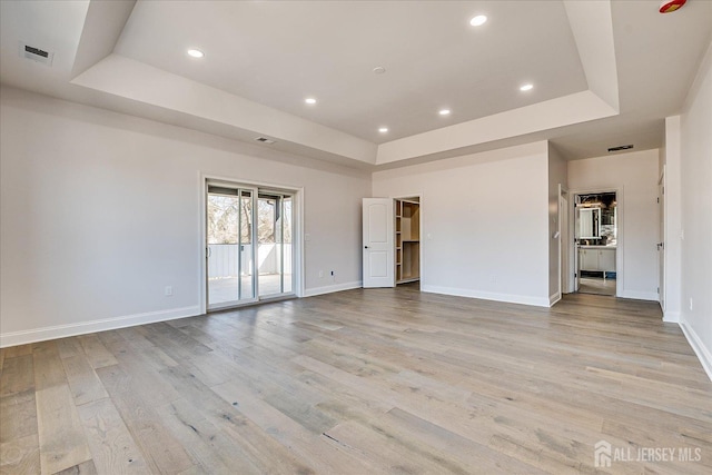 empty room with a raised ceiling, recessed lighting, light wood-style floors, and baseboards