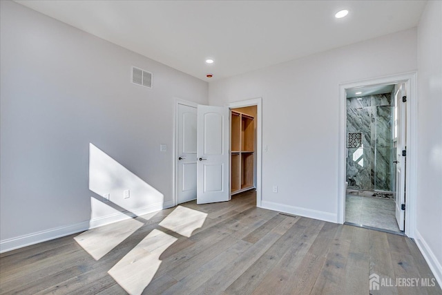 unfurnished bedroom with visible vents, a walk in closet, baseboards, and wood finished floors