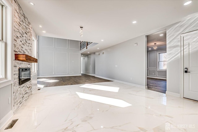 unfurnished living room featuring marble finish floor, heating unit, recessed lighting, a stone fireplace, and a decorative wall