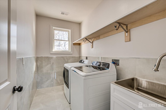 washroom featuring visible vents, washer and clothes dryer, a sink, tile walls, and laundry area