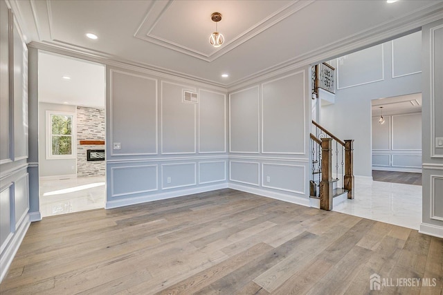 empty room with crown molding, stairs, a fireplace, light wood-style floors, and a decorative wall