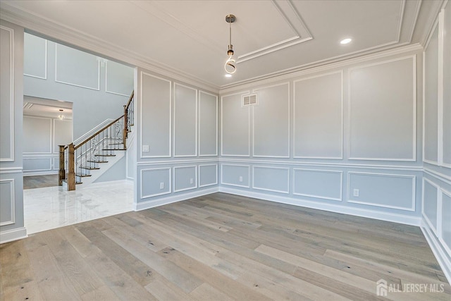 unfurnished room with visible vents, light wood-style flooring, crown molding, a decorative wall, and stairs