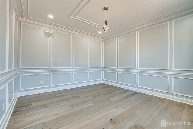 empty room featuring a decorative wall, light wood-style flooring, crown molding, and visible vents