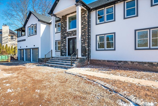 view of front of home featuring stucco siding, driveway, stone siding, french doors, and a garage