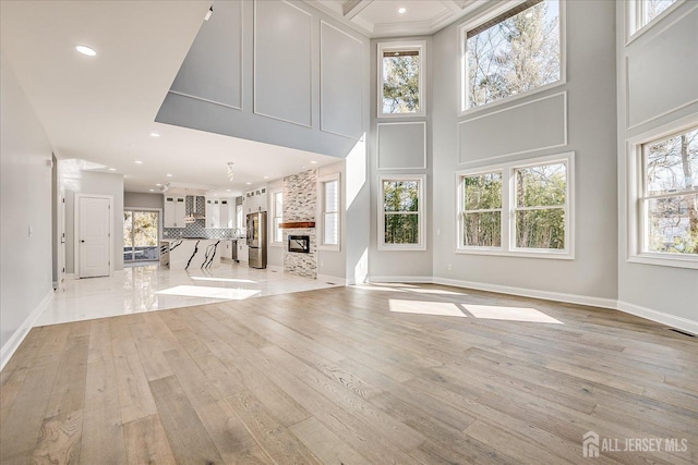 unfurnished living room featuring light wood-style flooring, recessed lighting, baseboards, and a high ceiling