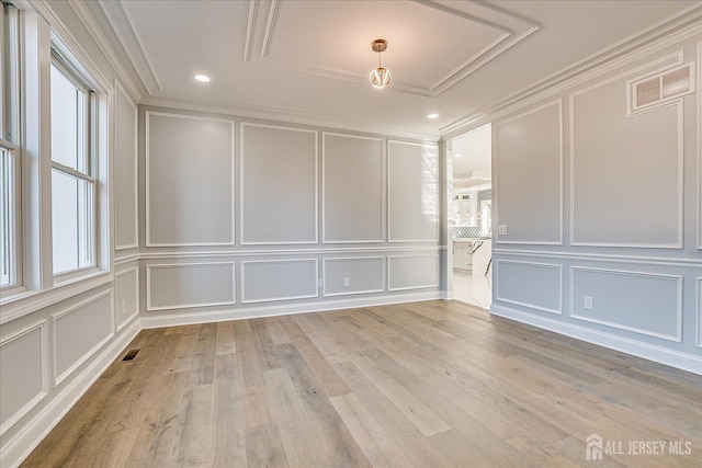 unfurnished room with light wood-type flooring, visible vents, ornamental molding, and a decorative wall