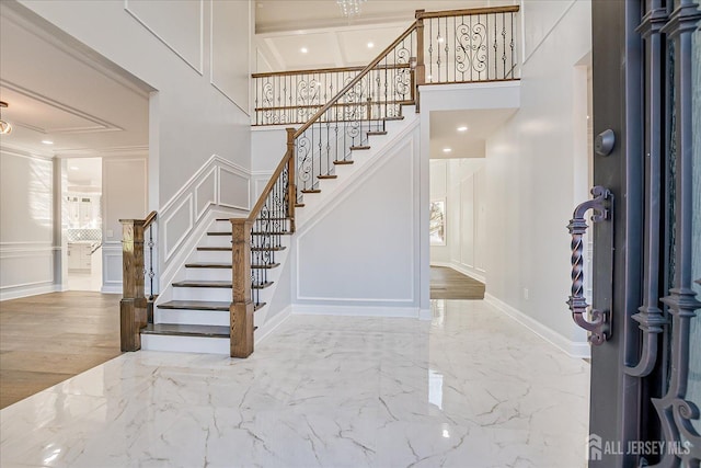 foyer featuring stairway, marble finish floor, ornamental molding, and a decorative wall