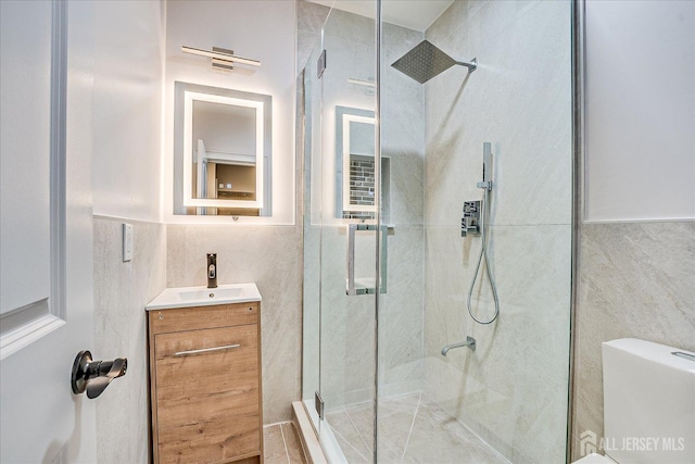 bathroom with toilet, a stall shower, tile walls, and vanity