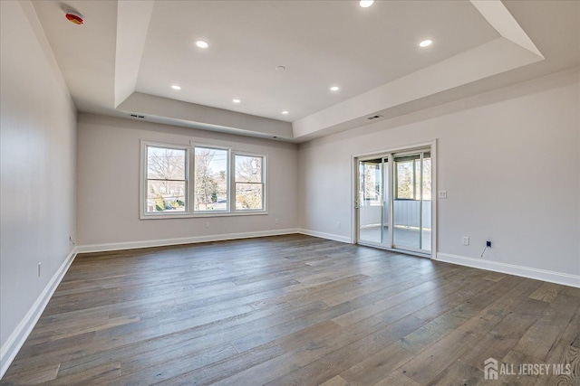 empty room featuring dark wood finished floors, recessed lighting, baseboards, and a tray ceiling