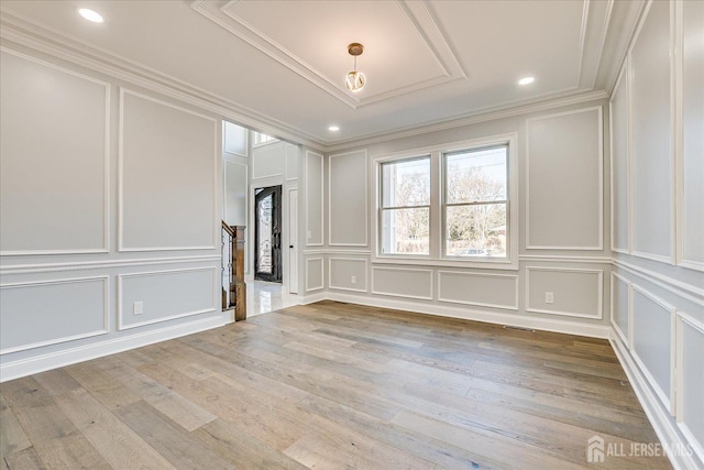 unfurnished room featuring a decorative wall, crown molding, light wood-type flooring, and stairs