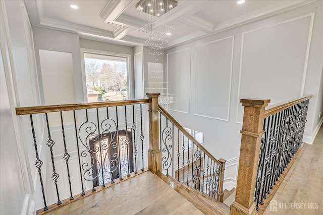 hall featuring wood finished floors, coffered ceiling, crown molding, a decorative wall, and an upstairs landing