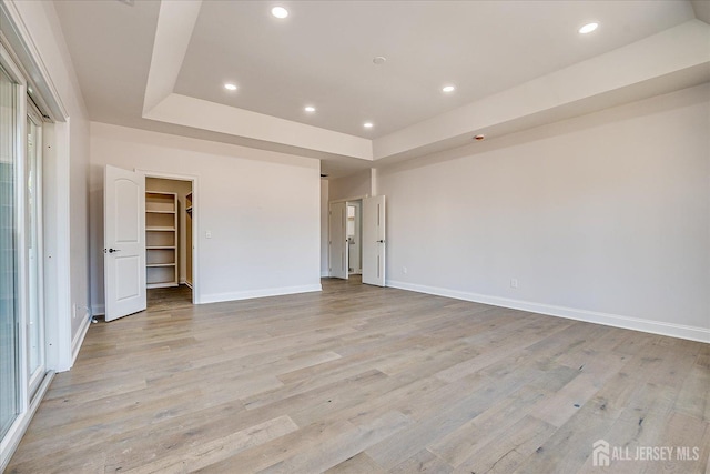 unfurnished room featuring a raised ceiling, recessed lighting, light wood-type flooring, and baseboards