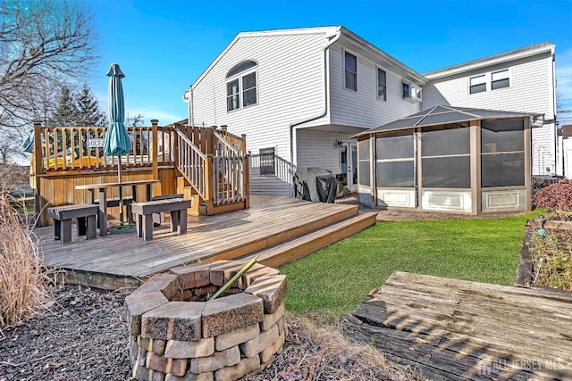 rear view of house with a lawn, a wooden deck, a sunroom, and a fire pit