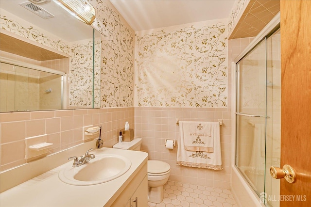 full bathroom featuring toilet, bath / shower combo with glass door, tile walls, vanity, and tile patterned flooring