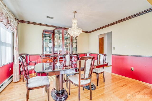 dining area with crown molding, a baseboard heating unit, an inviting chandelier, and light hardwood / wood-style flooring