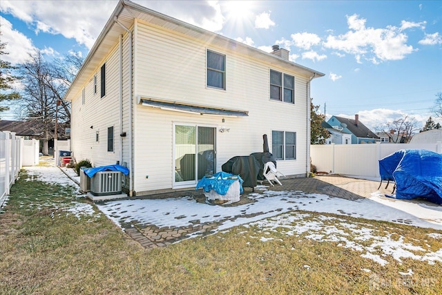 snow covered rear of property featuring a yard, a fenced backyard, a chimney, and cooling unit